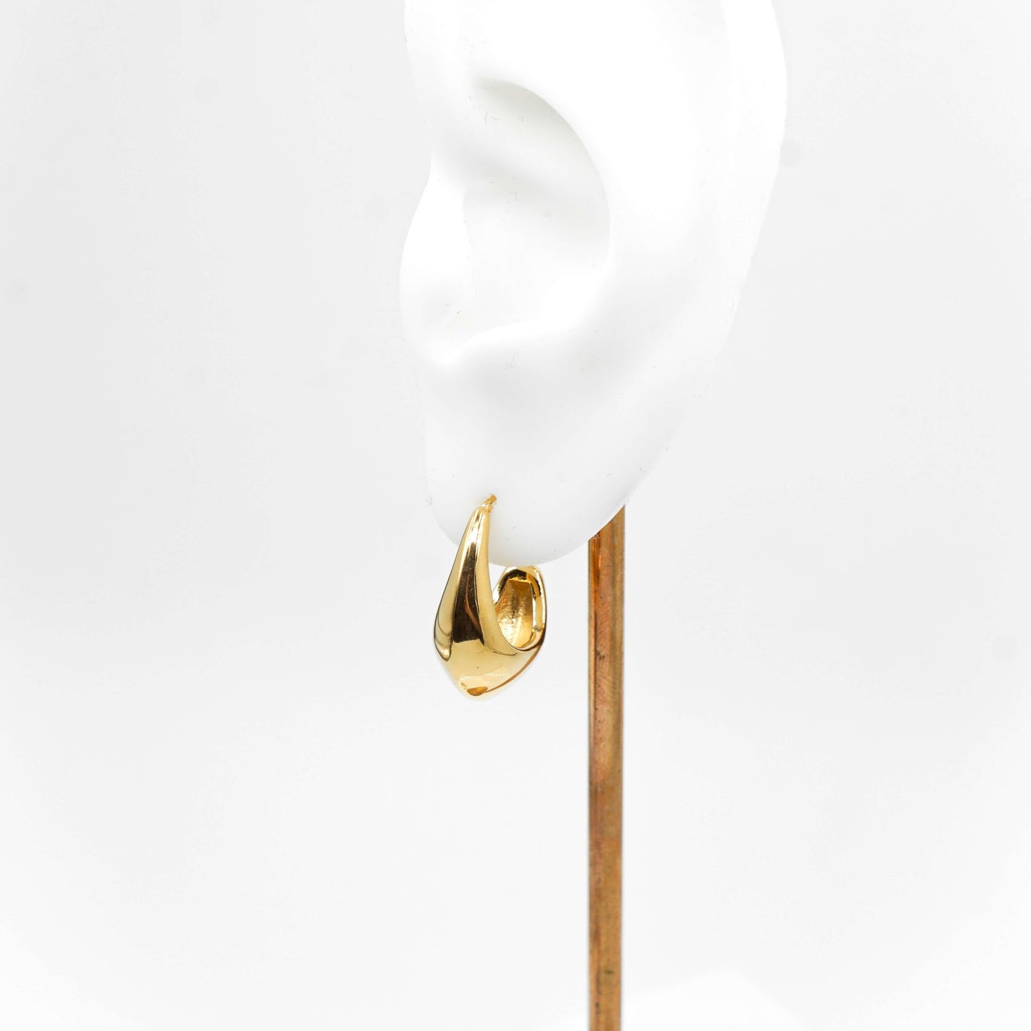 Korvakoru mallinukella. Korvakoru näyttää edestäpäin katsottuna kultaiselta pisaralta.